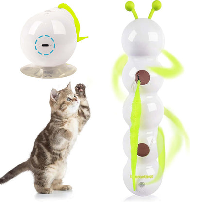 Curious kitten pawing at a white wall-mounted spinning smart cat toy with green feather and suction base for interactive play